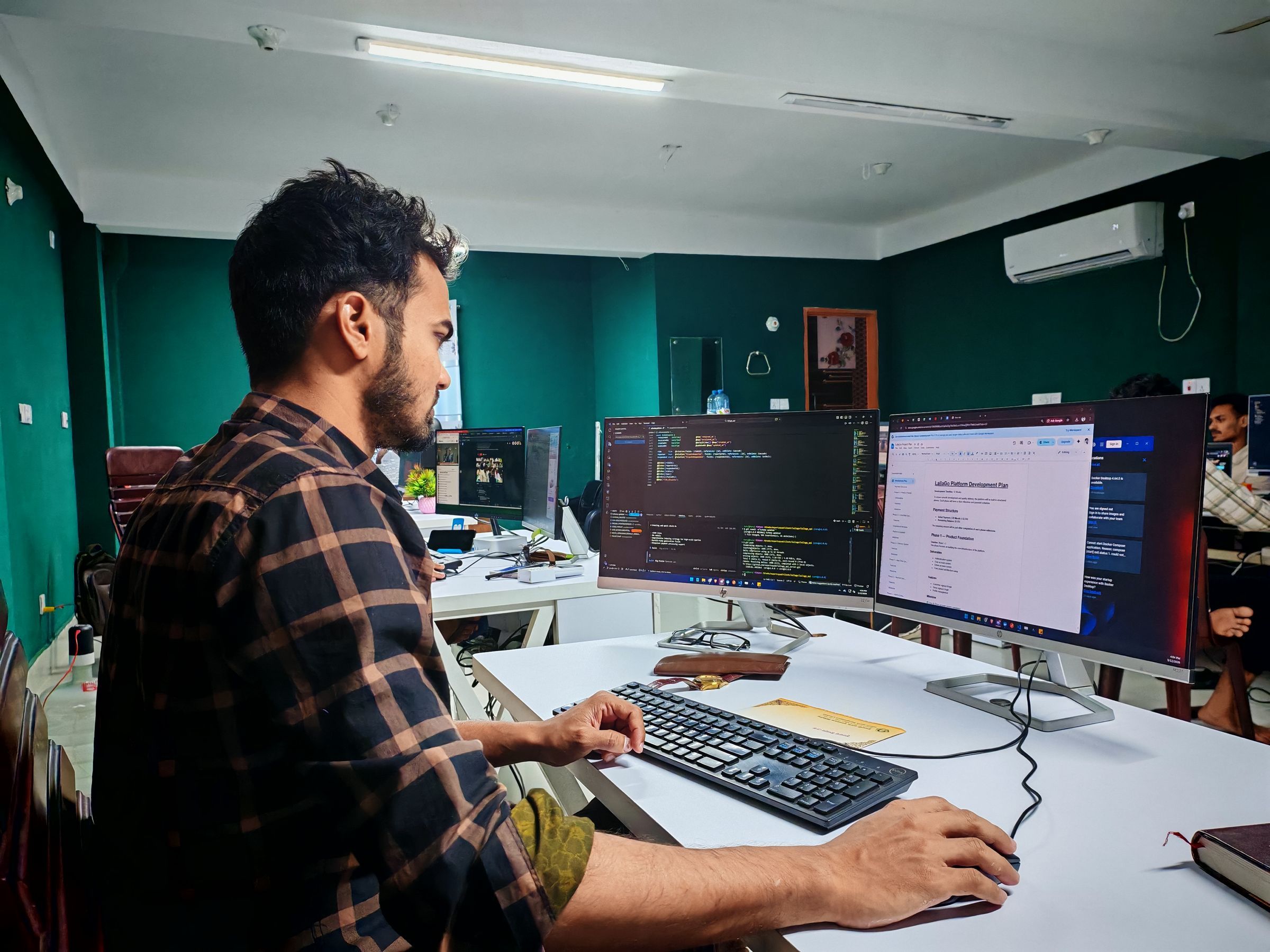 A developer working at two monitors in a bright office