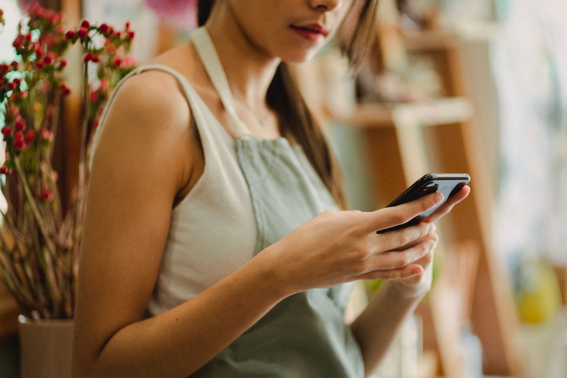 A shop owner in an apron reading a message on her phone in her flower shop