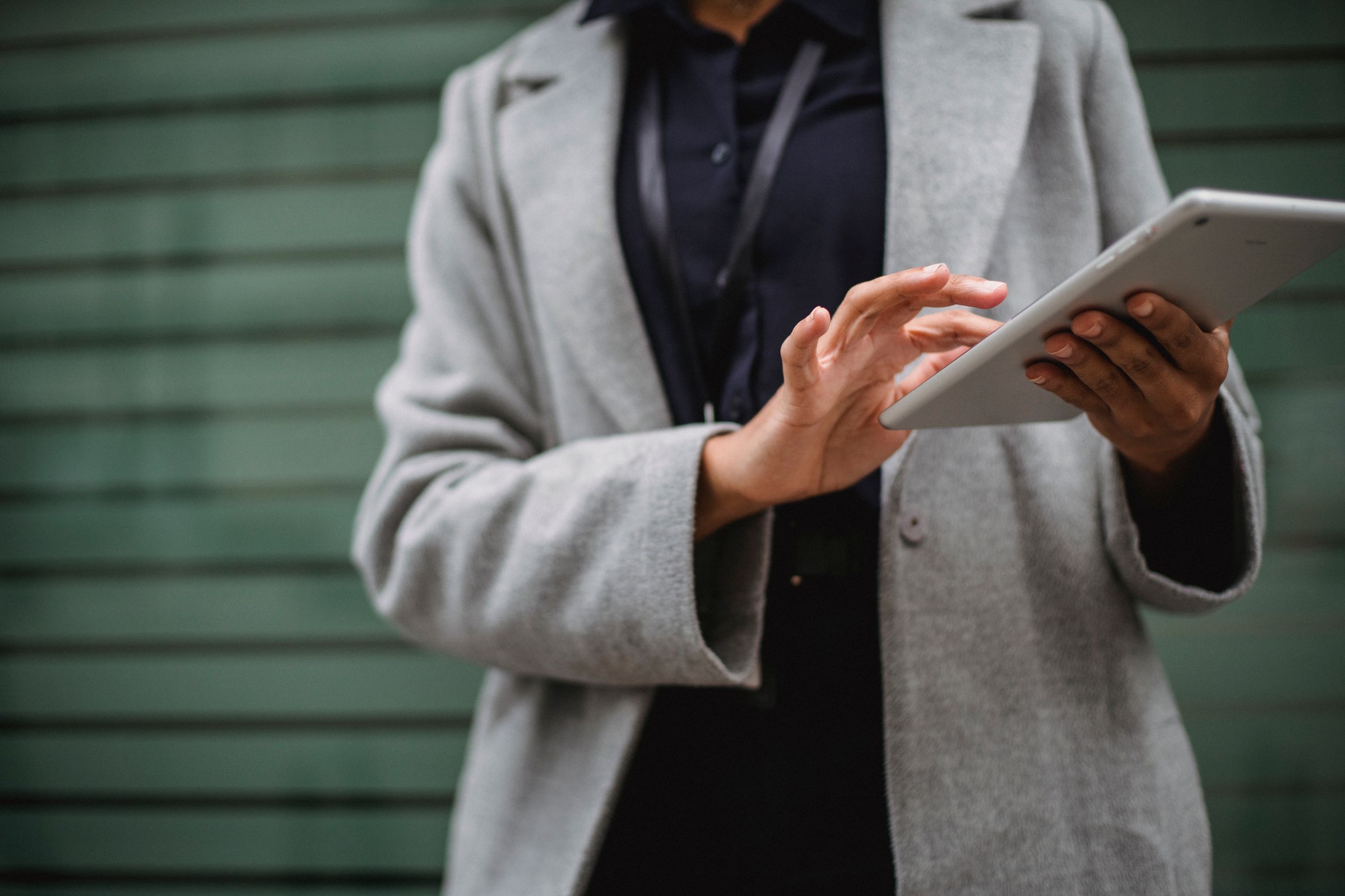 Hands in a grey coat working on a tablet