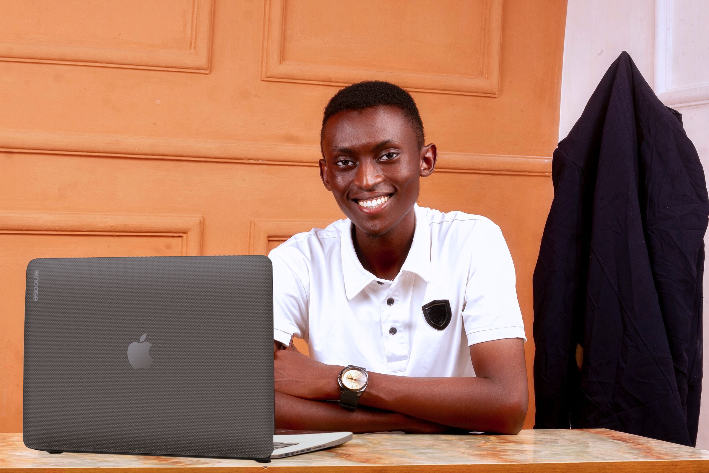 A young man smiling at his desk with a laptop